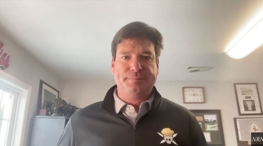 A man with short brown hair stands indoors wearing a dark jacket with a skull and crossed oars logo, featuring certificates and pictures on the wall behind him—capturing a vibe that's as inviting as Southern Cooking at Vicious Biscuit.
