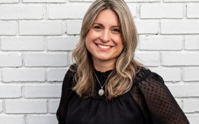 Woman with blonde hair wearing a black top, smiling in front of a white brick wall—full of flavor and perfect for a cheerful brunch moment.