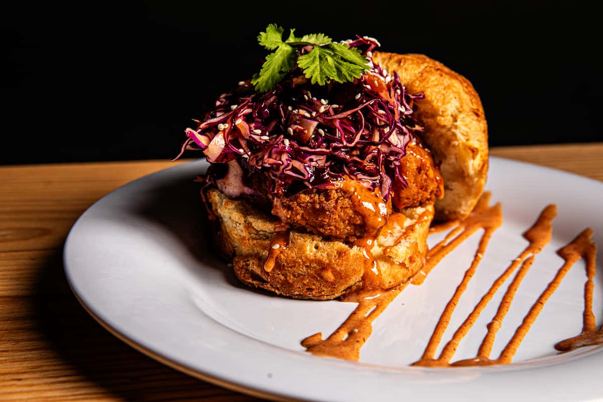 A fried chicken sandwich full of flavor, topped with red cabbage slaw and sauce, served on a white plate with artful sauce drizzles—a delicious nod to Southern cooking.